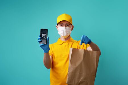 Courier with medical mask on his face holds bag and smartphone in his hand.