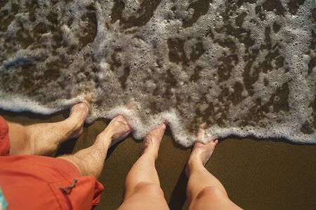 Top view on naked feets on sand in foaming sea wave.