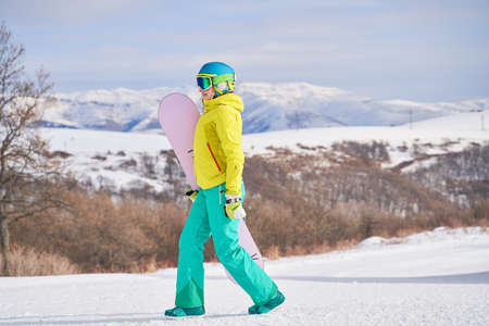 Woman with snowboard against background of mountainsの写真素材