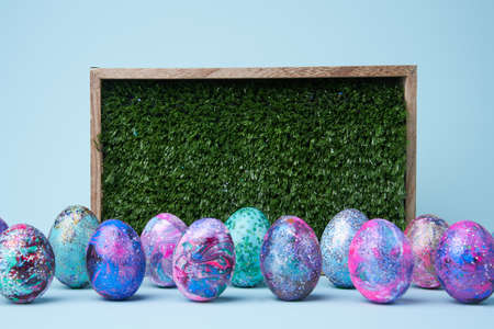 Colorful painted shiny eggs and wood box with grass, space for text.の写真素材