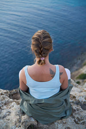Woman is siting on a rock, looking at the sea landscape, sunset and enjoying the view and fresh air.
