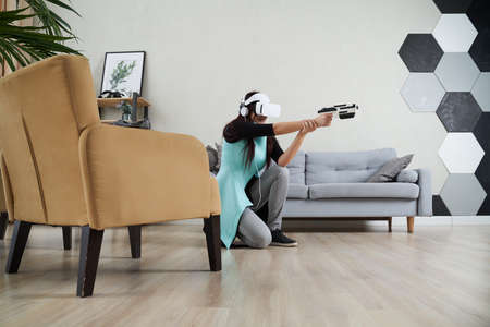 Woman with virtual reality headset and blaster is playing game.