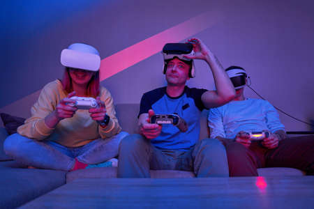 Friends playing virtual reality games using joysticks while sitting on the couch.