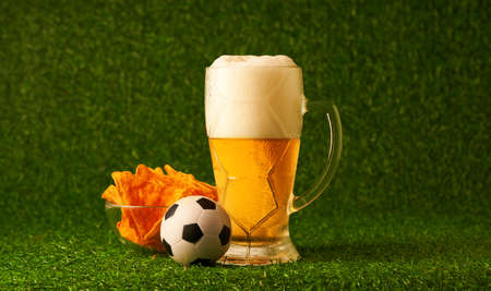 Glass of beer with soccer ball on the green grass background.の写真素材