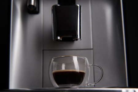 Freshly brewed coffee is poured from the coffee machine into glass cups.の写真素材