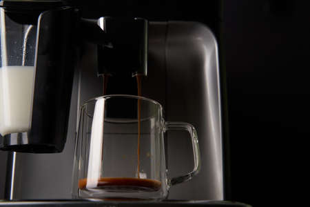 Freshly brewed coffee is poured from the coffee machine into glass cups.の写真素材