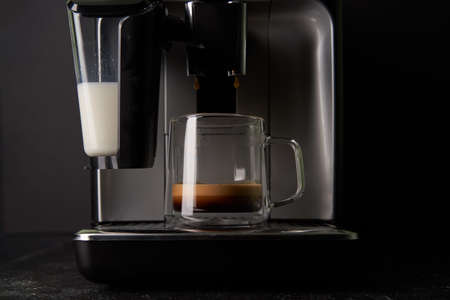 Freshly brewed coffee is poured from the coffee machine into glass cups.の写真素材