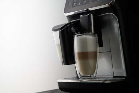 Freshly brewed latte is poured from the coffee machine into glass cups.の写真素材