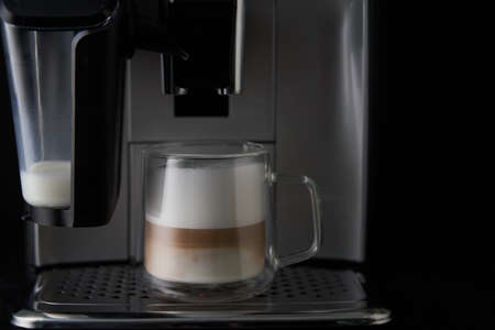 Freshly brewed cappuccino is poured from the coffee machine into glass cups.の写真素材