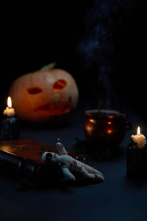Halloween pumpkin with burning mouths, book and a voodoo doll - volt on dark background.