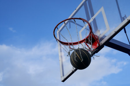 Street basketball ball falling into the hoop. Close up of black ball in the hoop net.の写真素材