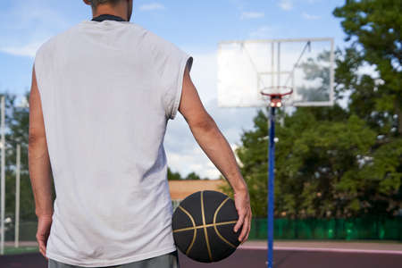 Man is standing with the ball in his hand on the background of the basketball court in the park.の写真素材