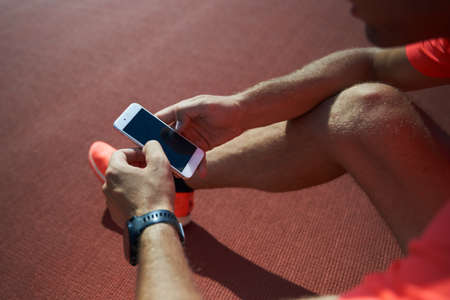 Sports man takes a break and relaxes after training or running around the stadium and using a...