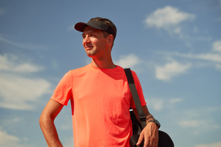 Male athlete with black bag on his shoulder stands near stadium waiting for training.の写真素材