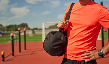 Male athlete with black bag on his shoulder stands near stadium waiting for training.の写真素材