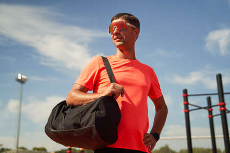 Male athlete with black bag on his shoulder stands near stadium waiting for training.の写真素材