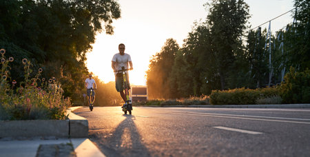 Mans are riding on electric scooters or e-scooters on the street on the sunset.