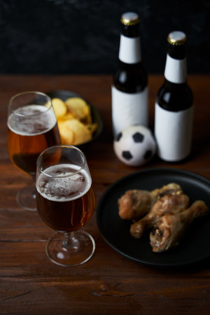 Two glasses with beer, bottles, snacks and soccer ball on wooden table.の写真素材