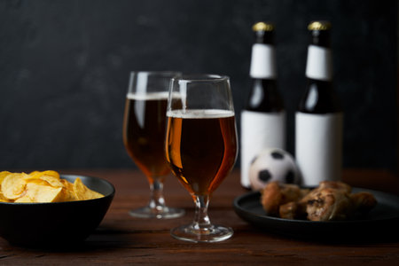 Two glasses with beer, bottles, snacks and soccer ball on wooden table.の写真素材