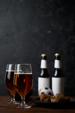 Two glasses with beer, bottles, snacks and soccer ball on wooden table.の写真素材