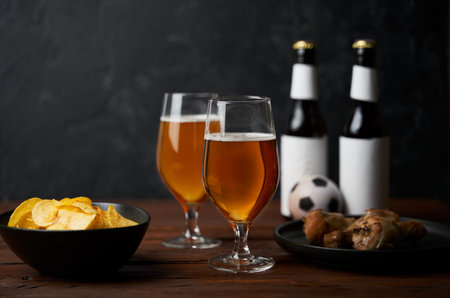Two glasses with beer, bottles, snacks and soccer ball on wooden table.の写真素材