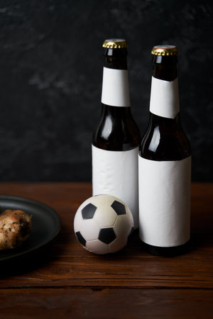 Two glasses with beer, bottles, snacks and soccer ball on wooden table.の写真素材