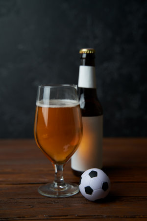 Two glasses with beer, bottles, snacks and soccer ball on wooden table.の写真素材