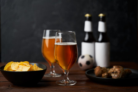 Two glasses with beer, bottles, snacks and soccer ball on wooden table.の写真素材