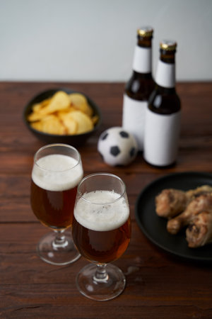 Two glasses with beer, bottles, snacks and soccer ball on wooden table.の写真素材