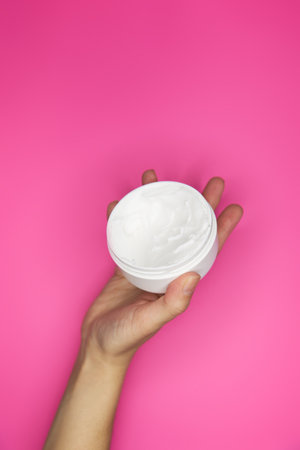 Female hands with jar of cream on pink backgroundの写真素材