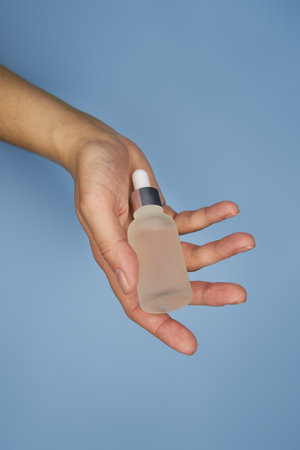 Female hands with serum in bottles on blue backgroundの写真素材