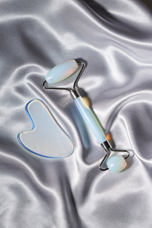 Blue jade face roller and Gua Sha scraping for beauty facial massage therapy on silver textured silk background.の写真素材