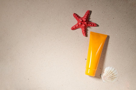 Summer sunscreen cream on sand background with starfish and shell.