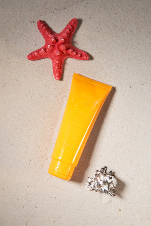 Summer sunscreen cream on sand background with starfish and shell.