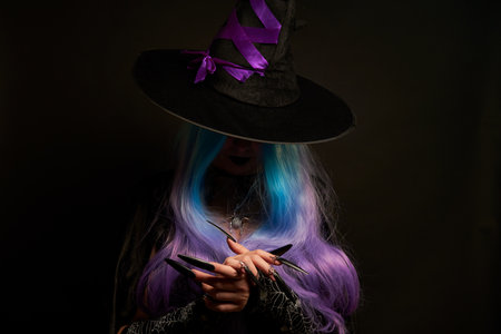 Halloween witch woman in black dress, cloak, black hat with violet ribbon, blue and violet hair and long black nails.の写真素材