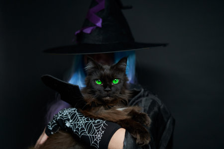 Witch with blue and violet hair, black hat with violet ribbon and long black nails is holding cat on her hands.の写真素材