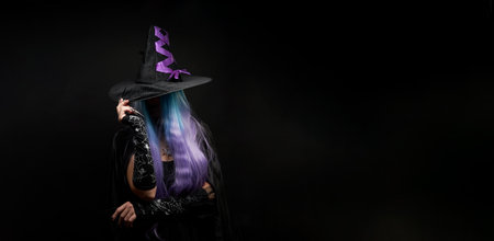 Halloween witch woman in black dress, cloak, black hat with violet ribbon, blue and violet hair and long black nails.の写真素材