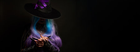 Halloween witch woman in black dress, cloak, black hat with violet ribbon, blue and violet hair and long black nails.の写真素材