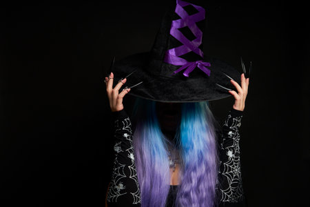 Halloween witch woman in black dress, cloak, black hat with violet ribbon, blue and violet hair and long black nails.の写真素材