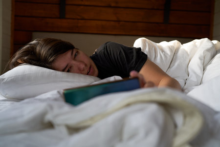 Woman in bed checking social media with smartphoneの写真素材