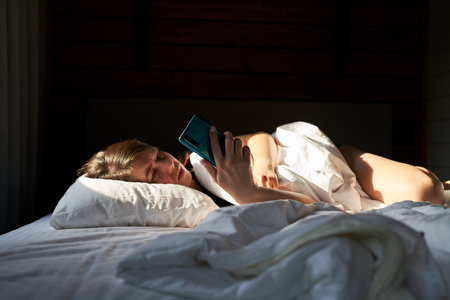 Woman in bed checking social media with smartphoneの写真素材