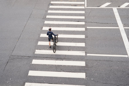 Man crosses the road at a pedestrian crossing and carries a bicycle next to him. View from above.の写真素材