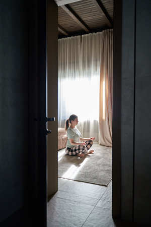 Woman Meditating in Sunlit Room Viewed Through Doorwayの写真素材