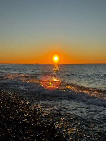 Sunset over ocean waves with golden reflections on pebble beachの写真素材