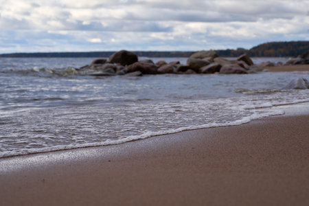 Gentle waves rolling toward sandy coast with visible rocks in foreground.の写真素材