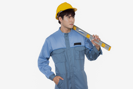 Portrait of young construction worker wearing yellow helmet in a Uniform mechanic is holding level isolated over white backgroundの写真素材