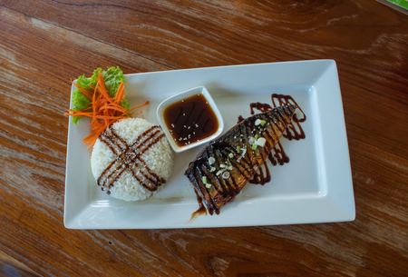 Rice and grilled saba sauce on a white plate on a wooden table.の写真素材