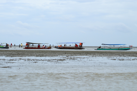A boat of tourists over the sea and Tourists looking for Snail shells on floor mud at Don Hoi lot in Samut songkham , Thailand 15 July 2018.のeditorial素材