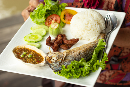 Rice, chili sauce, fish and pork fried with vegetables on a white plateの写真素材