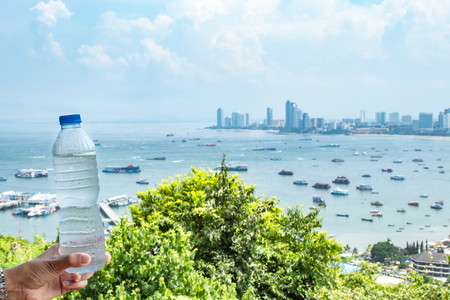 Hand holding Cold water and sea with many boats at Pattaya in Thailand.の写真素材